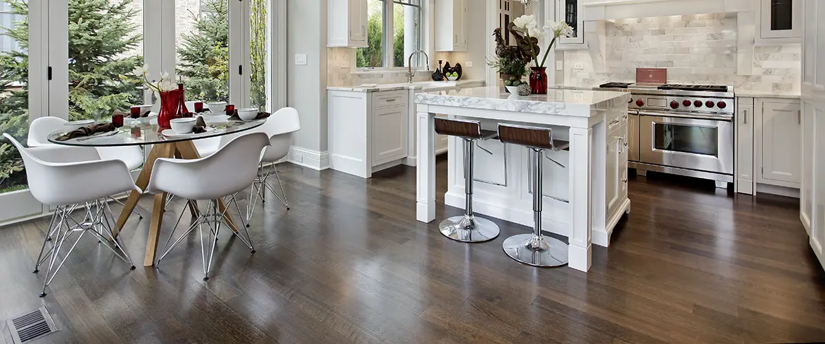 Bright modern kitchen in Alpharetta with white cabinets, marble countertops, island with bar stools, glass dining table, and large windows.