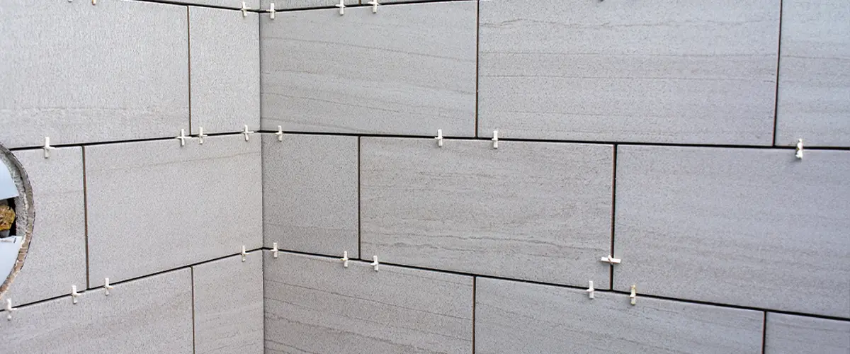 Close-up of gray ceramic tile installation in Alpharetta, on a wall using plastic tile spacers for precise alignment.