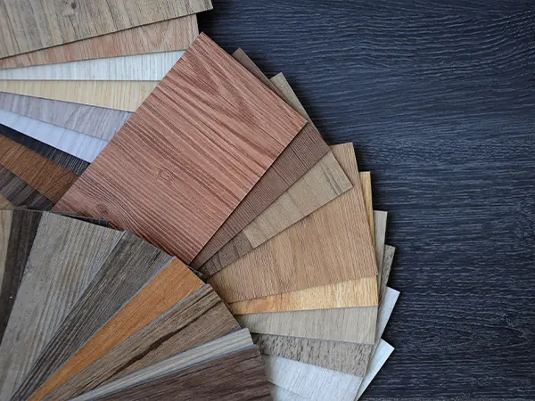 Collection of various laminate flooring samples in different wood finishes and shades displayed on a dark surface.