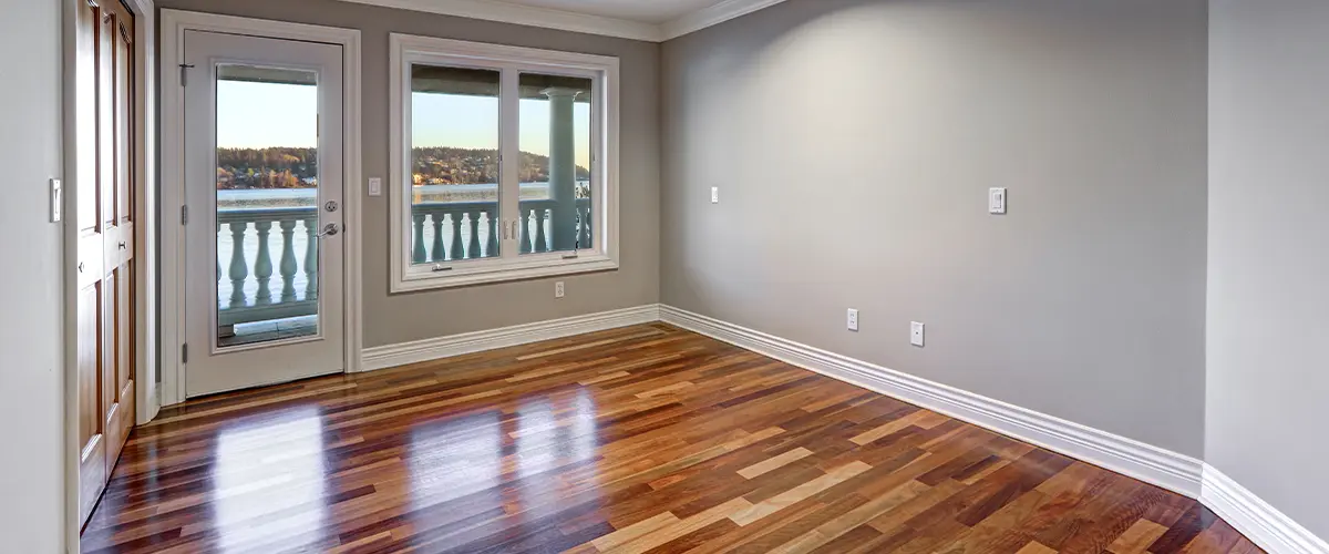 Empty room with hardwood flooring in Alpharetta, large windows, and a door leading to a balcony with water views. Gray walls and white trim