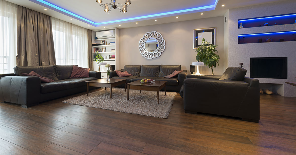 Modern living room in Alpharetta, with dark hardwood flooring, black leather sofas, blue LED ceiling lights, and a stylish mirror on the wall.