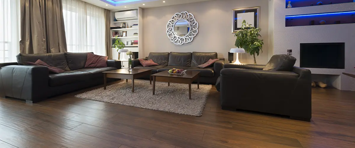 Modern living room in Alpharetta, with dark hardwood flooring, black leather sofas, blue LED ceiling lights, and a stylish mirror on the wall.