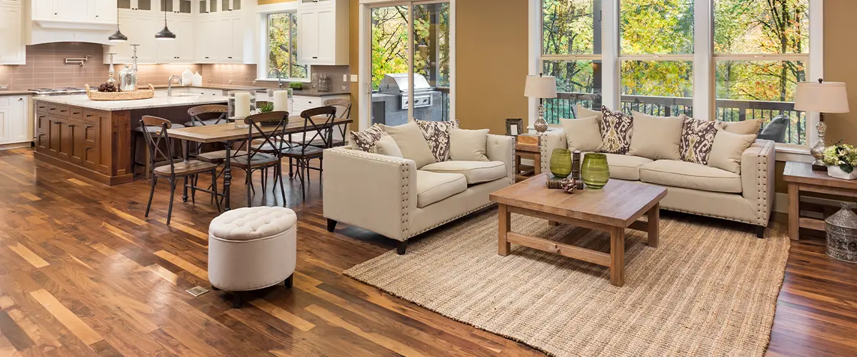 Modern open-concept living room and kitchen in Alpharetta, with hardwood flooring, beige sofas, wooden coffee table, and large windows.