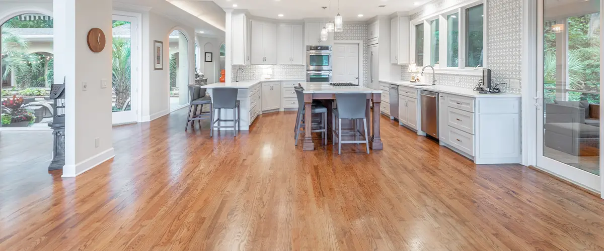 Spacious modern kitchen in Alpharetta, with hardwood floors, white cabinets, island seating, and large windows, open to a lush outdoor view.