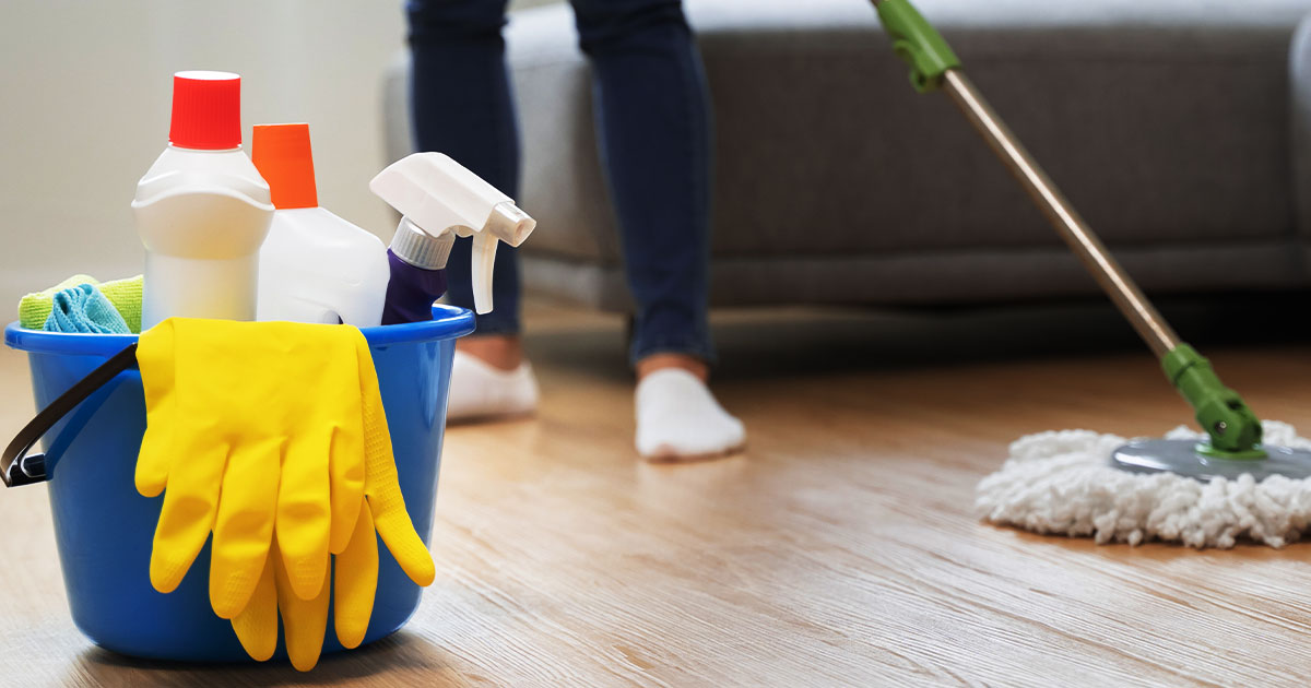 Close-up of a blue cleaning bucket with supplies and a person mopping a hardwood floor