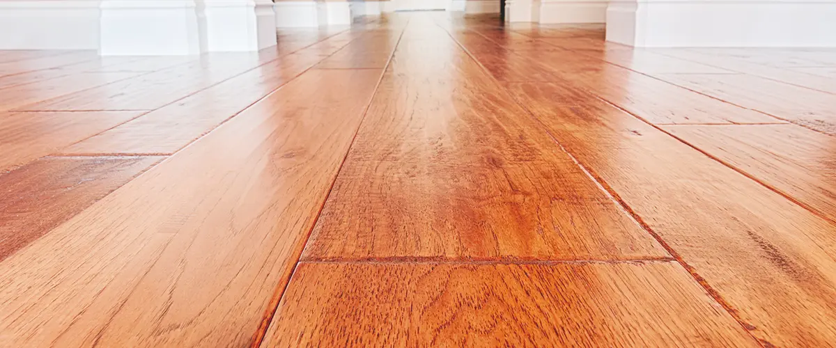 Close-up view of a newly refinished hardwood floor in a hallway with white baseboards