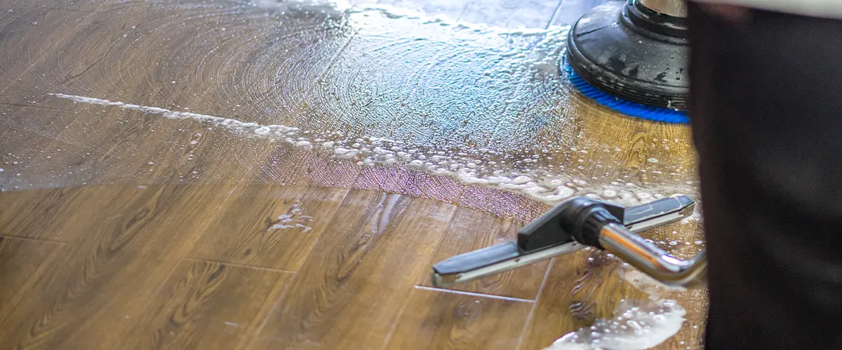 Professional floor cleaning with a machine and vacuum on a wooden surface covered in soapy water