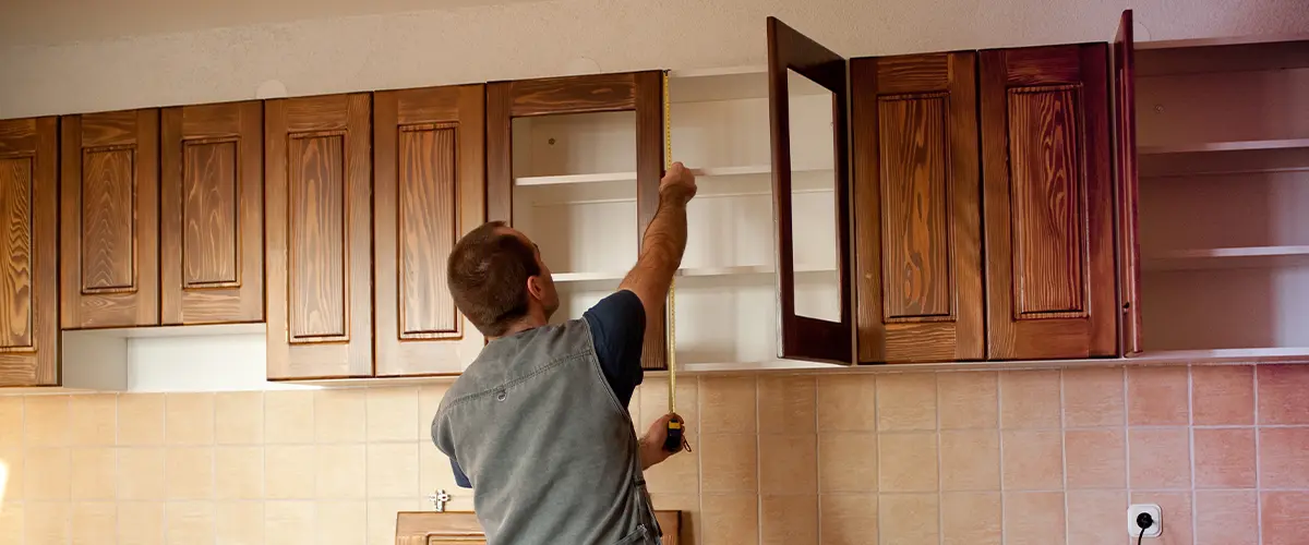 Worker measuring the height for new wooden kitchen cabinets during installation.