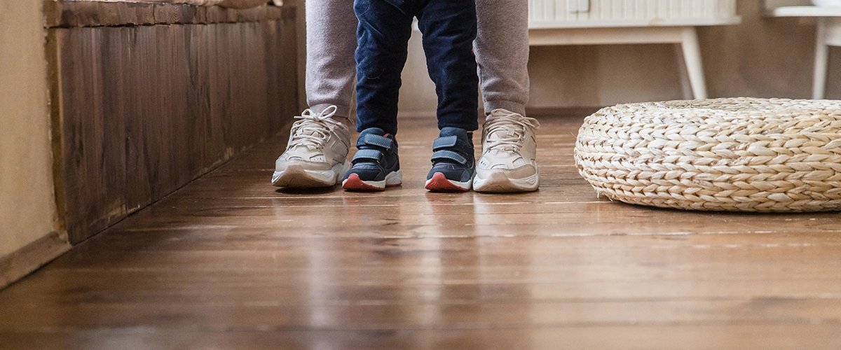 Legs of parent, son standing at home on wood floor heating