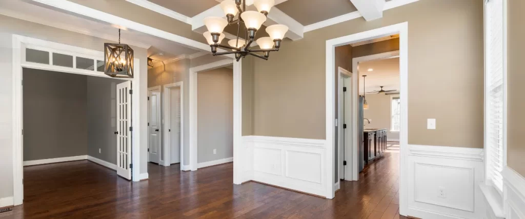 Spacious living area with hardwood flooring, a chandelier, and decorative wall paneling.