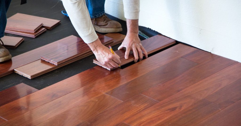 Worker installing hardwood flooring by aligning and securing wooden planks.