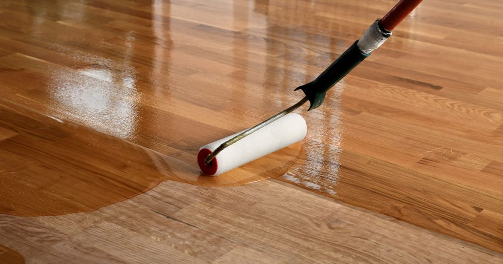 Roller applying protective finish on hardwood floor during professional wood floor refinishing and sealing