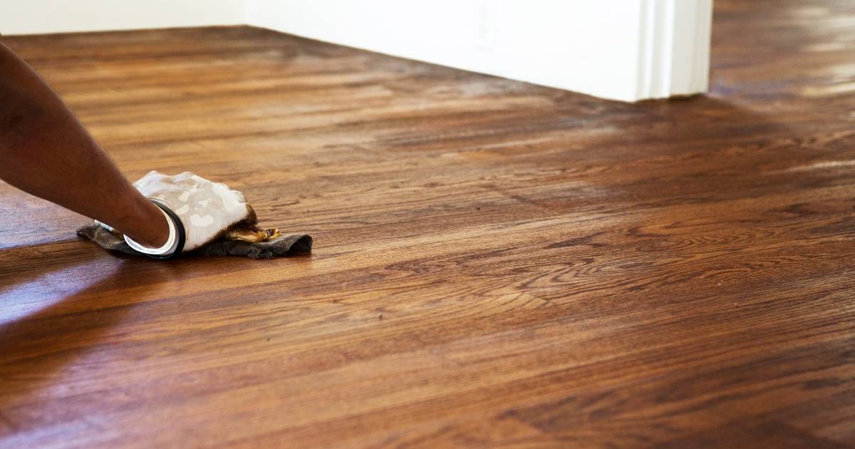 Applying dark wood stain to a hardwood floor during refinishing.