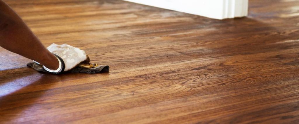 Close-up of hardwood floor being stained with a brush.